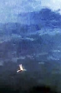 Frau in heller Kleidung liegt auf dem Rücken und schaut nach oben in den Himmel, umgeben von einer dunklen, wolkigen Atmosphäre.